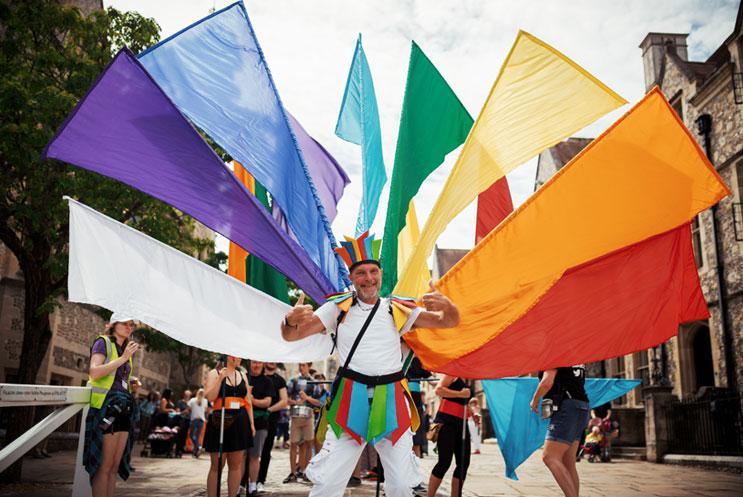 A man wearing multicoloured flags on his back, leading a parade.